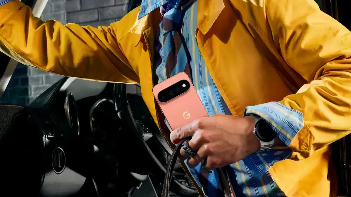 Persona con chaqueta amarilla bajando de un auto mientras sostiene en su mano el nuevo Google Pixel 11 color coral.